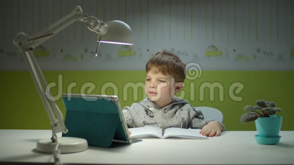用平板电脑做在线作业的学龄前男孩坐在书桌边和孩子们一起在线学习的孩子视频的预览图