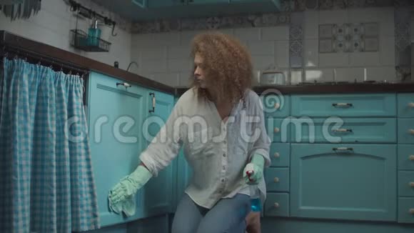年轻卷曲的20岁女性在清洁手套喷洒洗涤剂和擦拭厨房橱柜与抹布一个疲惫的女人视频的预览图