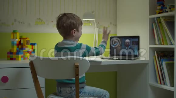 学龄前男孩在笔记本电脑屏幕上与男老师一起做在线学校作业坐在书桌前的孩子视频的预览图