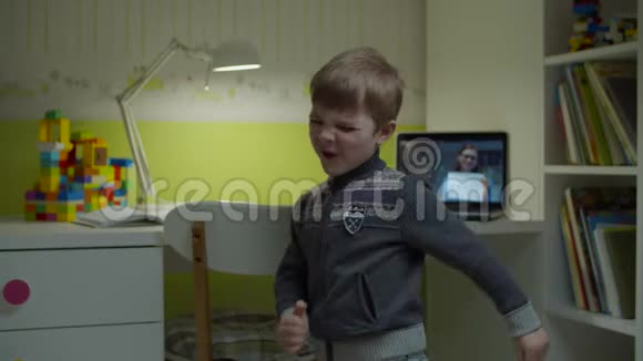 学龄前男孩在家跳舞带着笔记本电脑上的女老师上在线课网上学习快乐儿童舞蹈视频的预览图