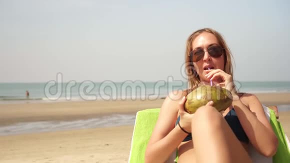 美丽的女人在海上休息在海滩上晒太阳喝椰子视频的预览图