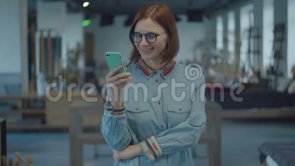 年轻的30多岁的黑发女人穿着民族衬衫和眼镜站着笑着看着手中的手机女性视频的预览图