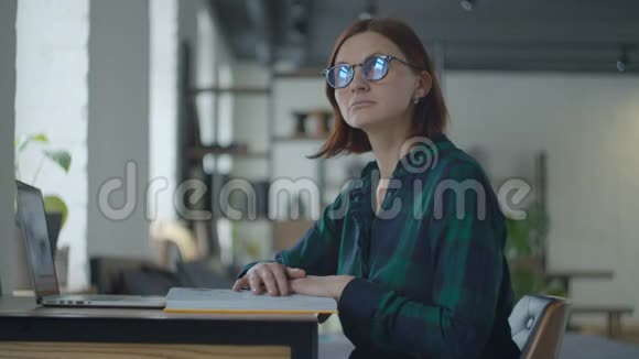 年轻的女成人戴眼镜坐在书桌前拿着相册和笔记本电脑学习想读书的女人视频的预览图