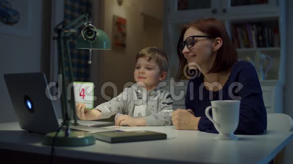 30多岁的妈妈在家和学龄前的儿子一起做网络作业小男孩在笔记本电脑屏幕上显示正确答案视频的预览图