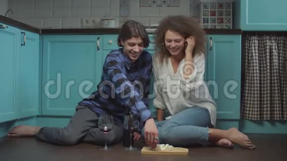 年轻的20多岁的夫妇在厨房的地板上喝酒吃奶酪快乐的微笑男人和女人庆祝视频的预览图
