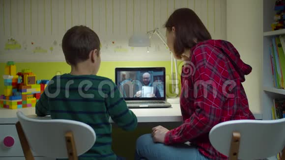 在笔记本电脑屏幕上与男老师在线上课时男生与妈妈一起做作业网上在线视频的预览图