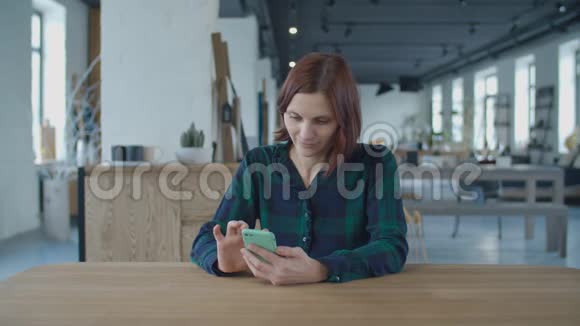 30多岁的年轻女工坐在有窗户的大房间的木桌旁用手机上网女人视频的预览图