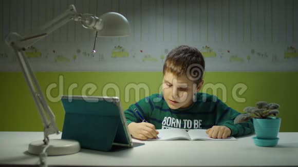小学生用平板电脑做在线作业孩子坐在书桌前在儿童室上网学习视频的预览图