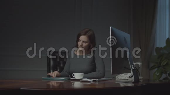 年轻的女商人晚上在商务办公室工作平板电脑坐在舒适的办公室里喝咖啡的女人视频的预览图