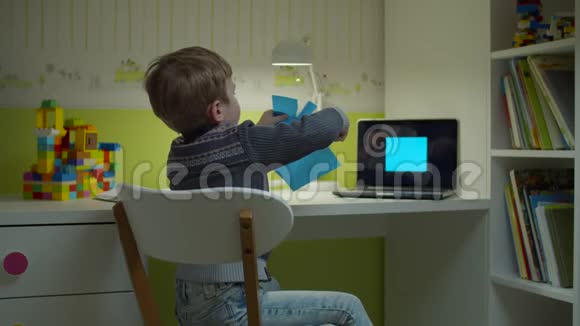学龄前男孩做在线艺术作业小孩用剪刀剪蓝色的方形坐在儿童桌旁视频的预览图