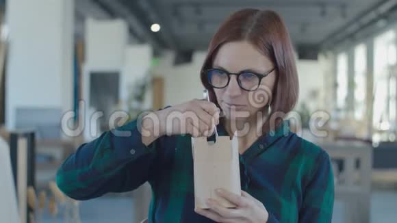 饥肠辘辘的女工从纸盒里吃午饭在笔记本电脑上看有趣的内容女人在桌子上吃面条视频的预览图