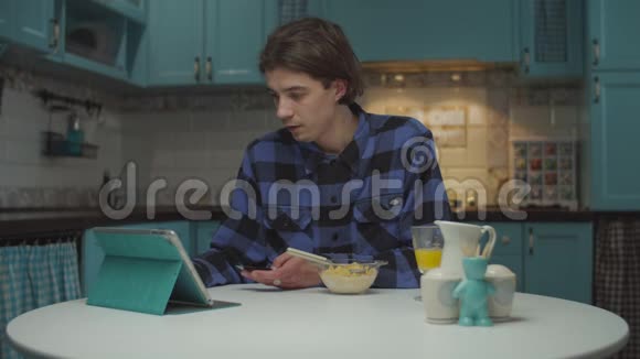 20多岁的年轻人独自吃早餐在蓝色厨房的平板电脑上上网购物男性购买视频的预览图