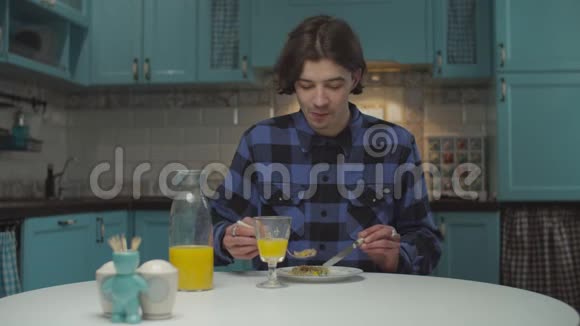 20多岁的年轻人独自在厨房吃饭男在家吃晚饭喝橙汁视频的预览图