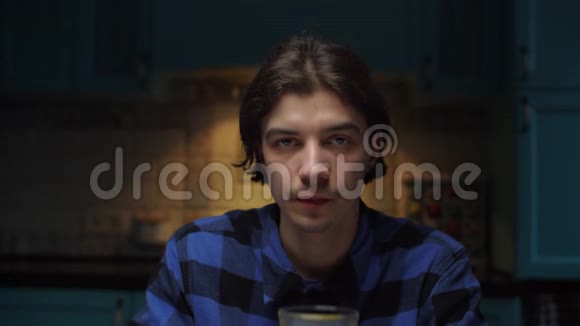 20多岁的年轻人喝着橙汁看着坐在黑暗房间里的摄像机穿蓝色衬衫的男士喝一杯水果视频的预览图