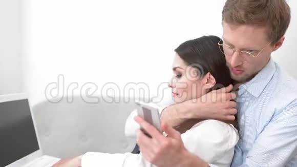 男人在电话上浏览社交网络而他的女性在一个工作日后卧床休息视频的预览图