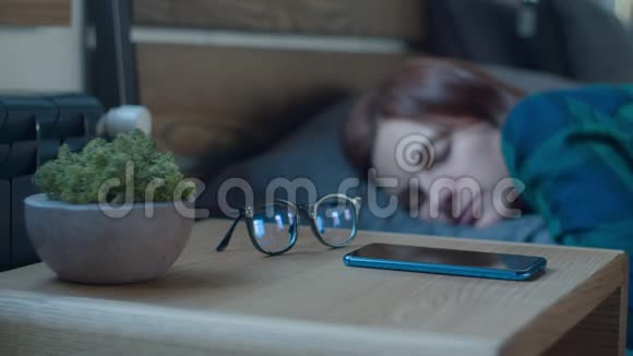 熟睡的女性醒来时手机上挂着闹钟床头柜上放着苔藓植物和眼镜女人手视频的预览图
