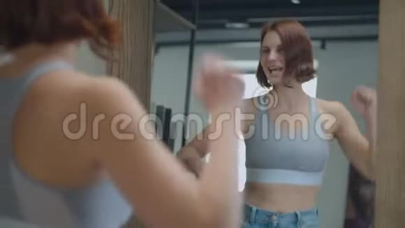 30多岁的年轻女性穿着大尺寸的旧牛仔裤欣赏减肥的结果快乐的女人在镜子里跳舞视频的预览图