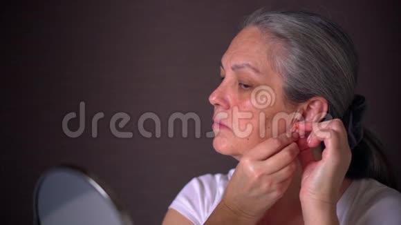 成熟的灰发女人试着耳环和镜子视频的预览图