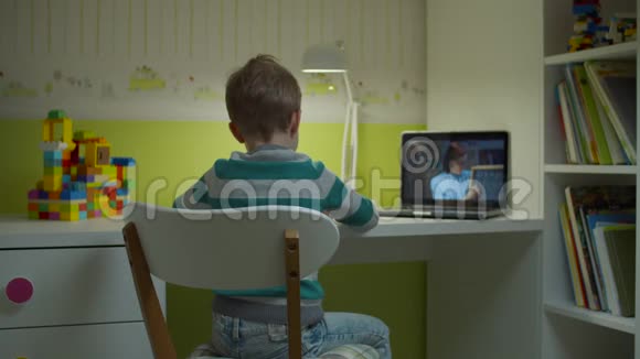 学龄前男孩与年轻的女教师在笔记本电脑屏幕上做在线学校作业坐在办公桌前的孩子视频的预览图