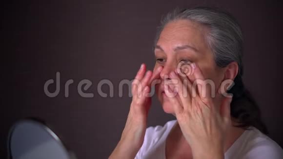 肖像高级妇女用保湿霜在她的脸上照镜子视频的预览图
