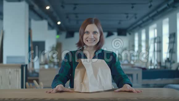 饥饿兴奋的女工坐在办公桌前拿着送食品的纸袋女人拿着午餐打开袋子闻着视频的预览图