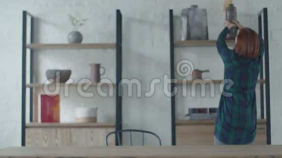 30多岁的年轻女性从架子上拿花瓶和盆子放在木桌上极简主义的室内公寓妇女视频的预览图