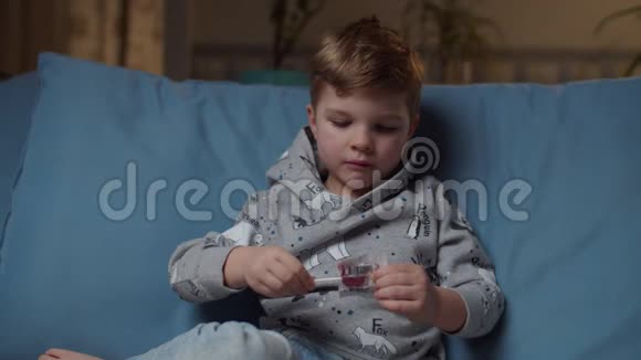 晚上坐在舒适的沙发上小男孩打开糖果把棒棒糖带到嘴里小孩喜欢吃硬糖视频的预览图