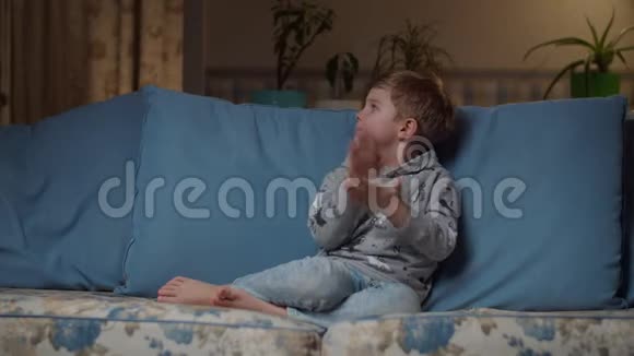 金发的学龄前男孩晚上坐在舒适的沙发上喝果汁妈妈给儿子端来一杯吸管孩子视频的预览图