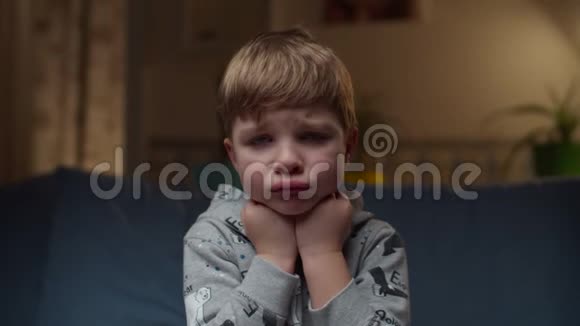 小男孩坐在家里的沙发上的肖像悲伤的孩子脸缓慢地看着摄像机视频的预览图