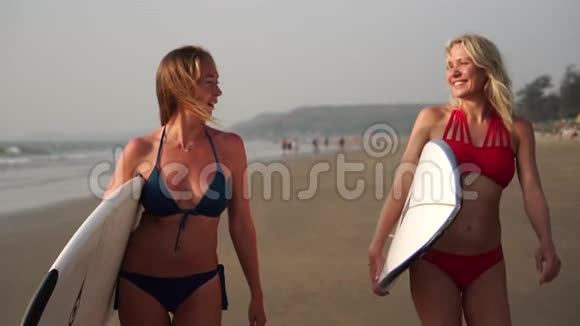 两个穿比基尼的性感女人带着冲浪板沿着海滩散步视频的预览图
