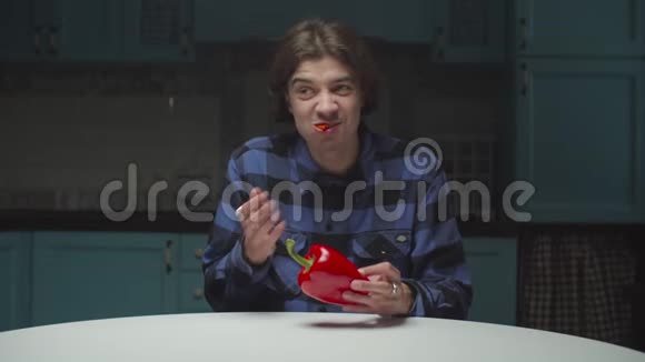 20多岁的年轻人在厨房里用滑稽的方式吃红辣椒嘴里含着辣椒的人不好吃有趣搞笑视频的预览图