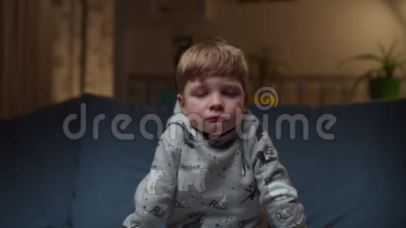 小男孩坐在家里的沙发上的肖像悲伤的孩子脸缓慢地看着摄像机视频的预览图