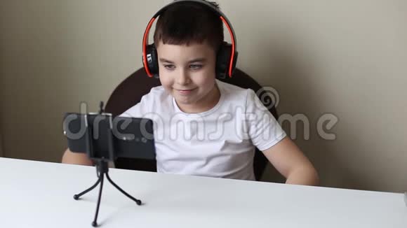 一个带着耳机的男孩微笑着看着智能手机视频的预览图