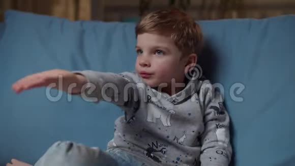 小男孩手拿糖果晚上坐在舒适的沙发上拿着棒棒糖到嘴边妈妈给我视频的预览图