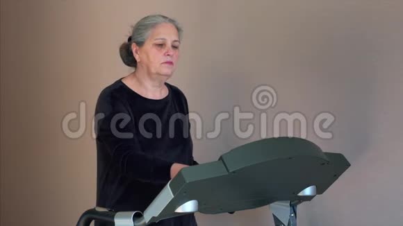 年长的白发妇女在家训练前改变了跑步机的模式视频的预览图