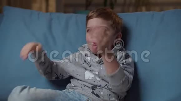 小男孩嘴里叼着棒棒糖晚上坐在舒适的沙发上给他妈妈五个妈妈鼓掌视频的预览图