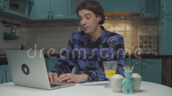 年轻的20多岁的商人通过笔记本电脑在线交谈并在蓝色厨房上展示纸质文件有纸的男企业家视频的预览图
