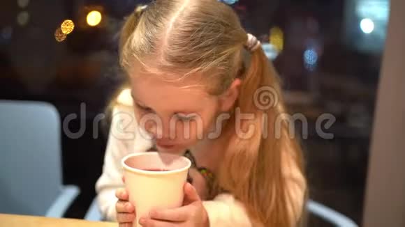 一个金发的小女孩晚上在咖啡馆喝热茶视频的预览图