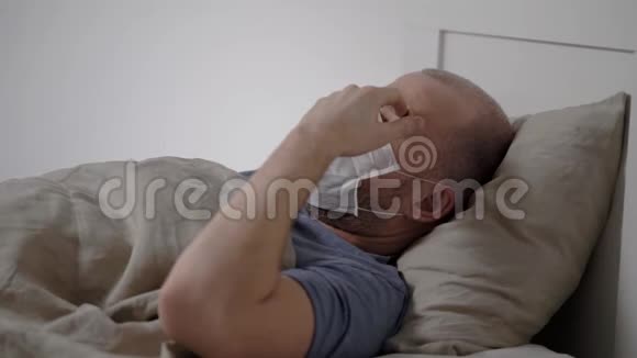 患有冠状病毒的19岁成年男子躺在卧室里嘴和鼻子上戴着医用口罩咳嗽视频的预览图