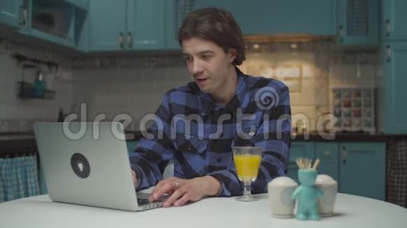 年轻的20多岁的男学生在家厨房的笔记本电脑上工作人很高兴在网上完成工作坐在视频的预览图