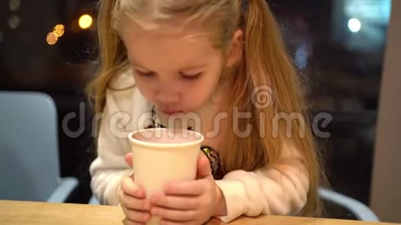 一个金发的小女孩晚上在咖啡馆喝热茶视频的预览图