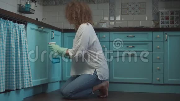 年轻卷曲的20岁女性在清洁手套喷洒洗涤剂和擦拭厨房橱柜与抹布一个疲惫的女人视频的预览图