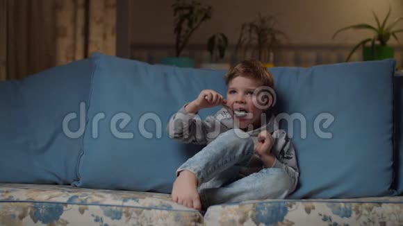金发的学龄前男孩晚上在舒适的沙发上吃午饭孩子吃白米饭玩勺子儿童视频的预览图