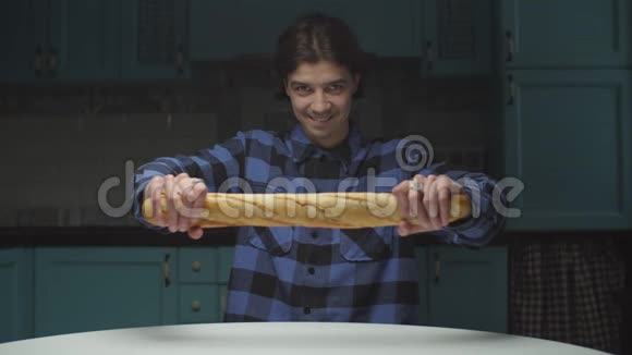 20多岁的年轻人在厨房里滑稽地吃着面包男人打破面包看着镜头微笑有趣搞笑视频的预览图