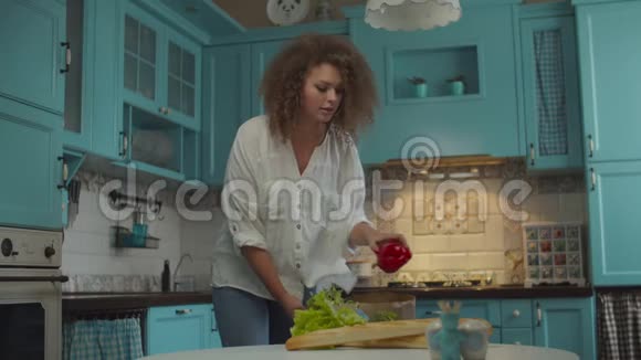 年轻的卷发20岁的女人拿着纸袋厨房里有新鲜的食物快乐的女性打开蔬菜和面包视频的预览图