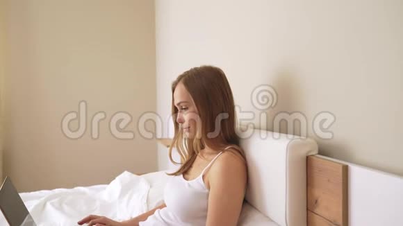 年轻女人在床上用笔记本电脑视频的预览图
