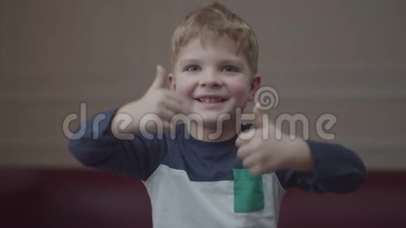金发的学龄前男孩微笑着竖起大拇指看着镜头年轻积极的孩子握手视频的预览图