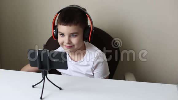 一个带着耳机的男孩微笑着看着智能手机视频的预览图