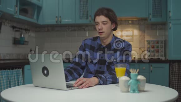 20多岁的男人厌倦了在家里厨房的笔记本电脑上工作男学生关闭笔记本电脑休息一下可怜的工人视频的预览图