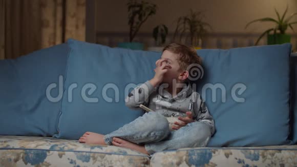 金发的学龄前男孩晚上在舒适的沙发上跪着一碗米饭孩子不吃食物穿牛仔裤的小孩视频的预览图